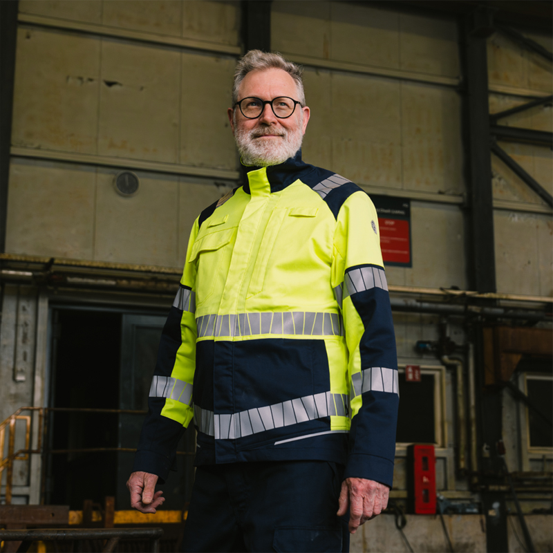 Mann trägt HaVeP Warnschutzjacke in Gelb und Marineblau mit Reflexstreifen in einer Industriehalle