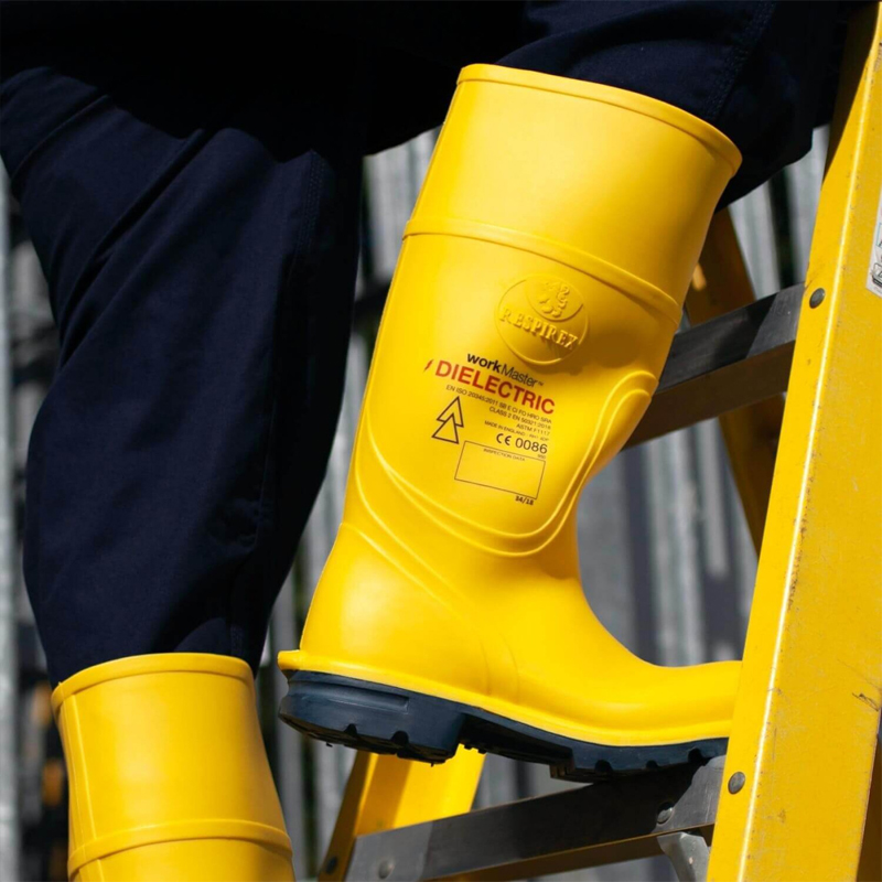 Person trägt gelbe BSD Sicherheitsstiefel, elektrisch isolierend bis 20 kV nach EN 50321 Klasse 2, beim Arbeiten auf einer Leiter