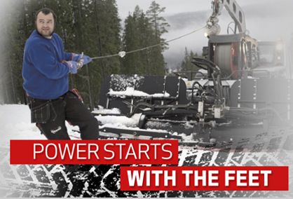 Werbebild: Mann bedient im Schnee eine Forstmaschine mit Fußstart im Wald, Slogan „Power Starts with the Feet“