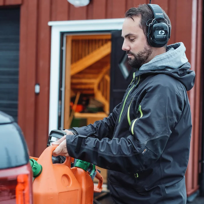 Mann trägt Wolf Protection Kapselgehörschutz und befüllt eine Motorsäge mit Kraftstoff vor einer Garage