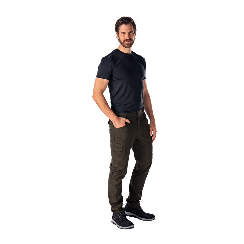 Mann trägt die Planam Herren Stretchy Hose mit 4-Wege-Stretch in Dunkeloliv in der Ganzkörperansicht, kombiniert mit dunkelblauem Shirt und Sportschuhen.