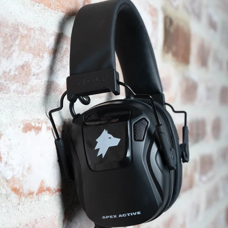 APEX ACTIVE Kapselgehörschutz in Schwarz mit gepolstertem Bügel und Wolf-Logo, seitlich an einer Ziegelwand hängend